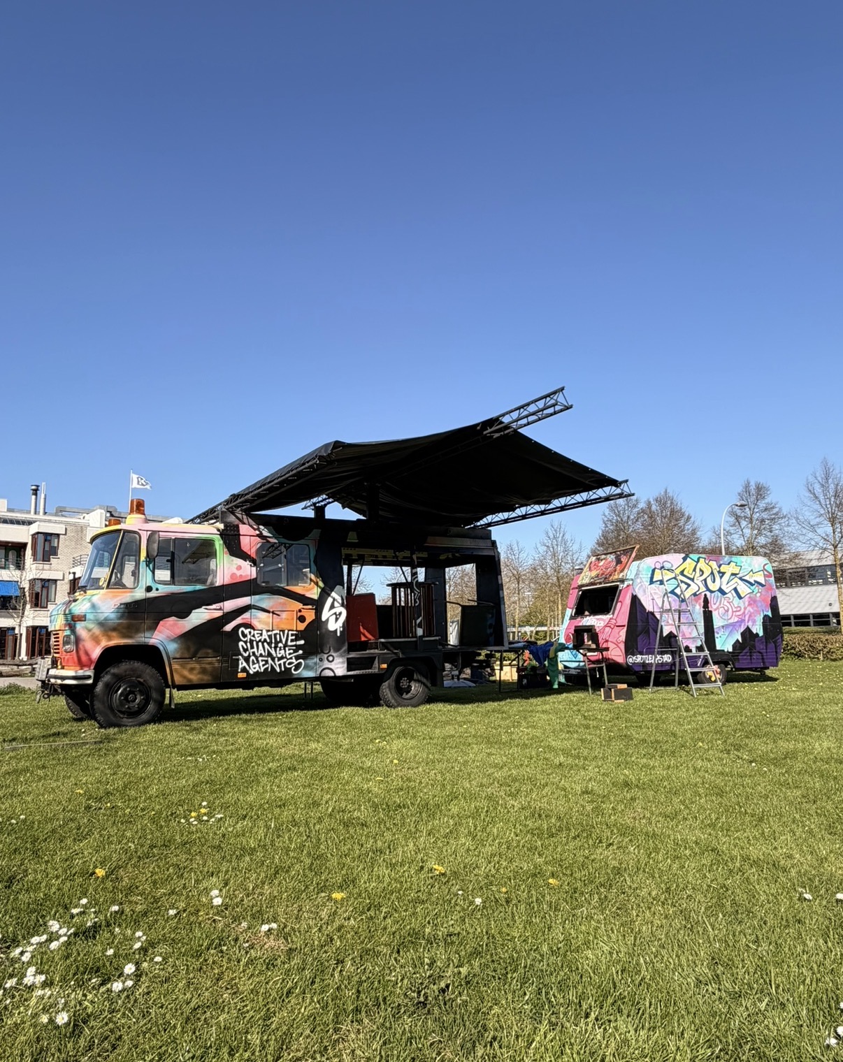 De kleurrijke SPOT! Talentenbus met open zijkant en overkapping op locatie, naast de SPOT!-caravan